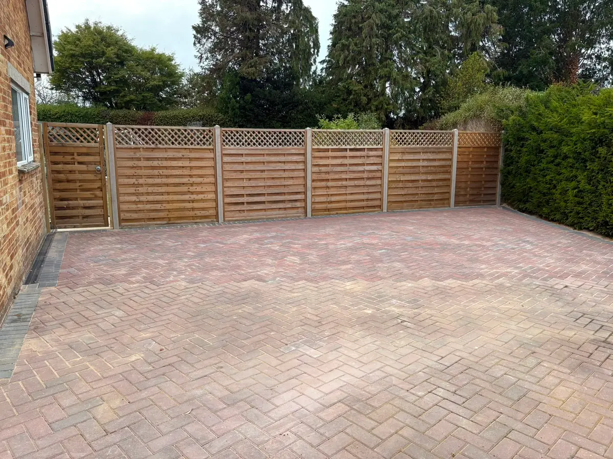 Finished block paved driveway in tumbled setts, enclosed by lattice-topped fence panels