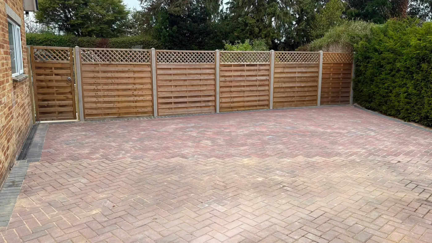 Finished block paved driveway in tumbled setts, enclosed by lattice-topped fence panels