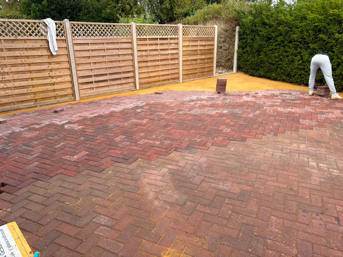 Curved block paved driveway edge running alongside lattice-topped fence panels and a clipped hedge