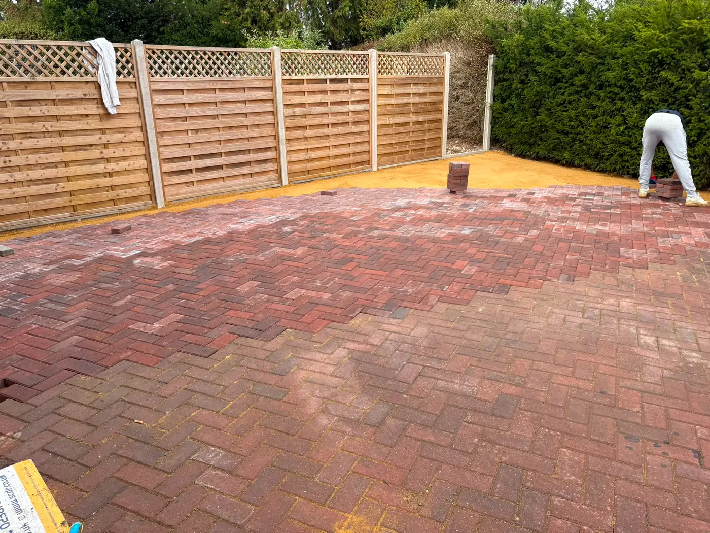 Curved block paved driveway edge running alongside lattice-topped fence panels and a clipped hedge