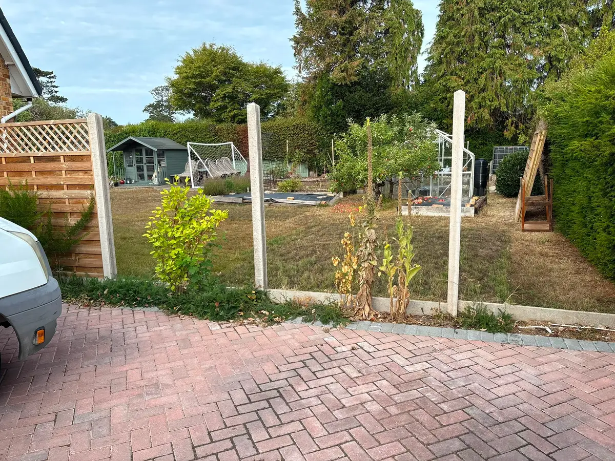 Completed block paved driveway with new fence posts and a garden beyond