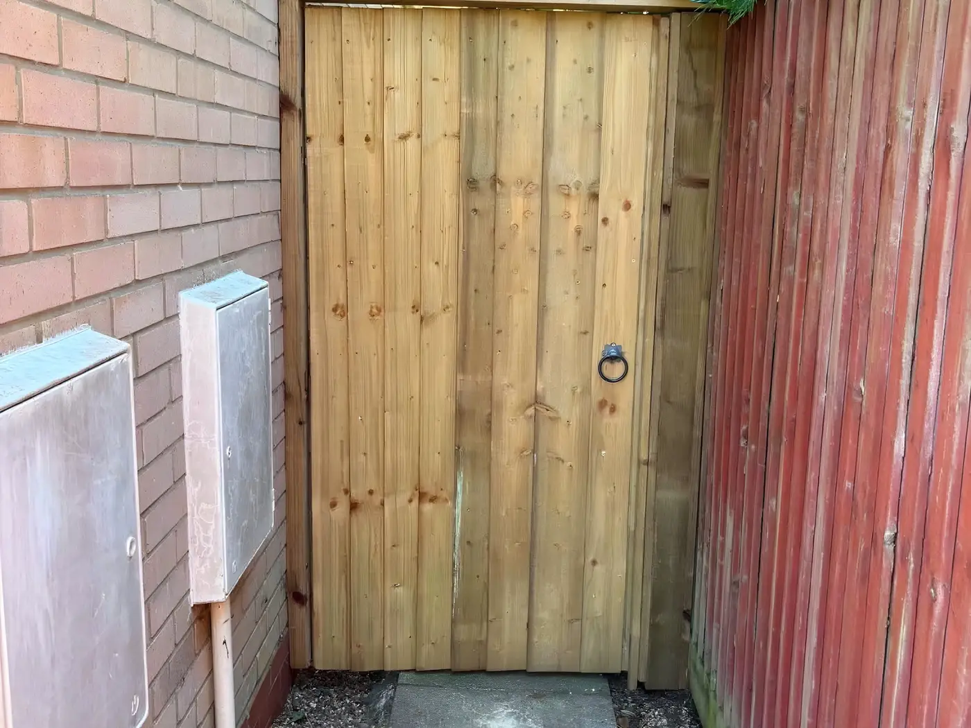 New closeboard timber gate fitted in a narrow alley between a brick wall and a fence