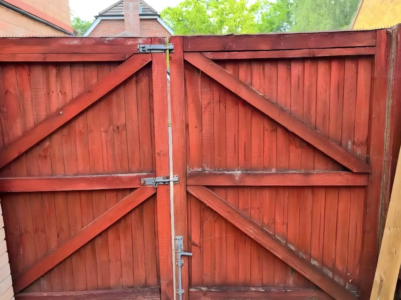 Braced timber double gates finished in a red stain, hung between fence panels