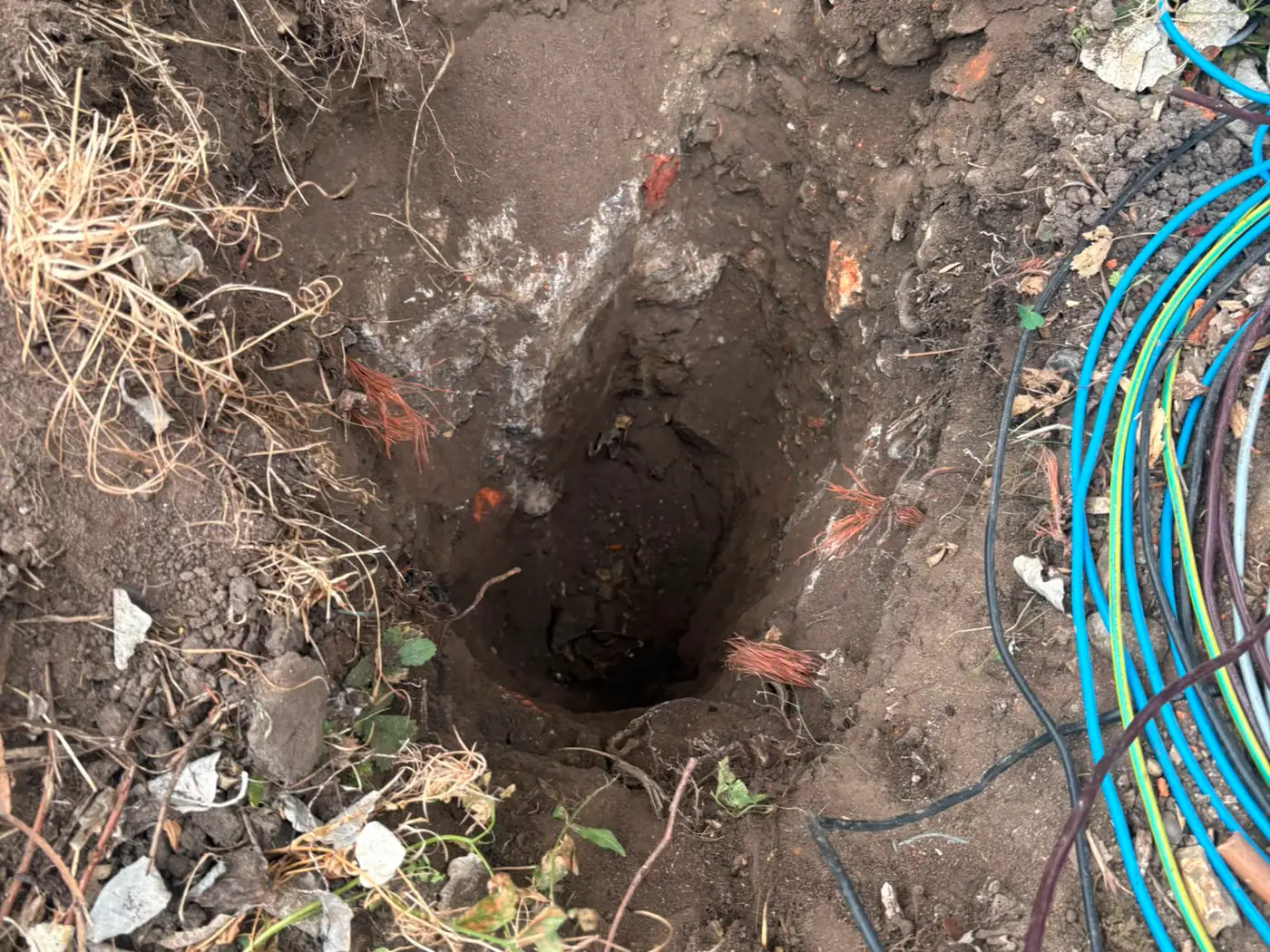 A hand dug hole exposing buried water and electricity services before excavation continues