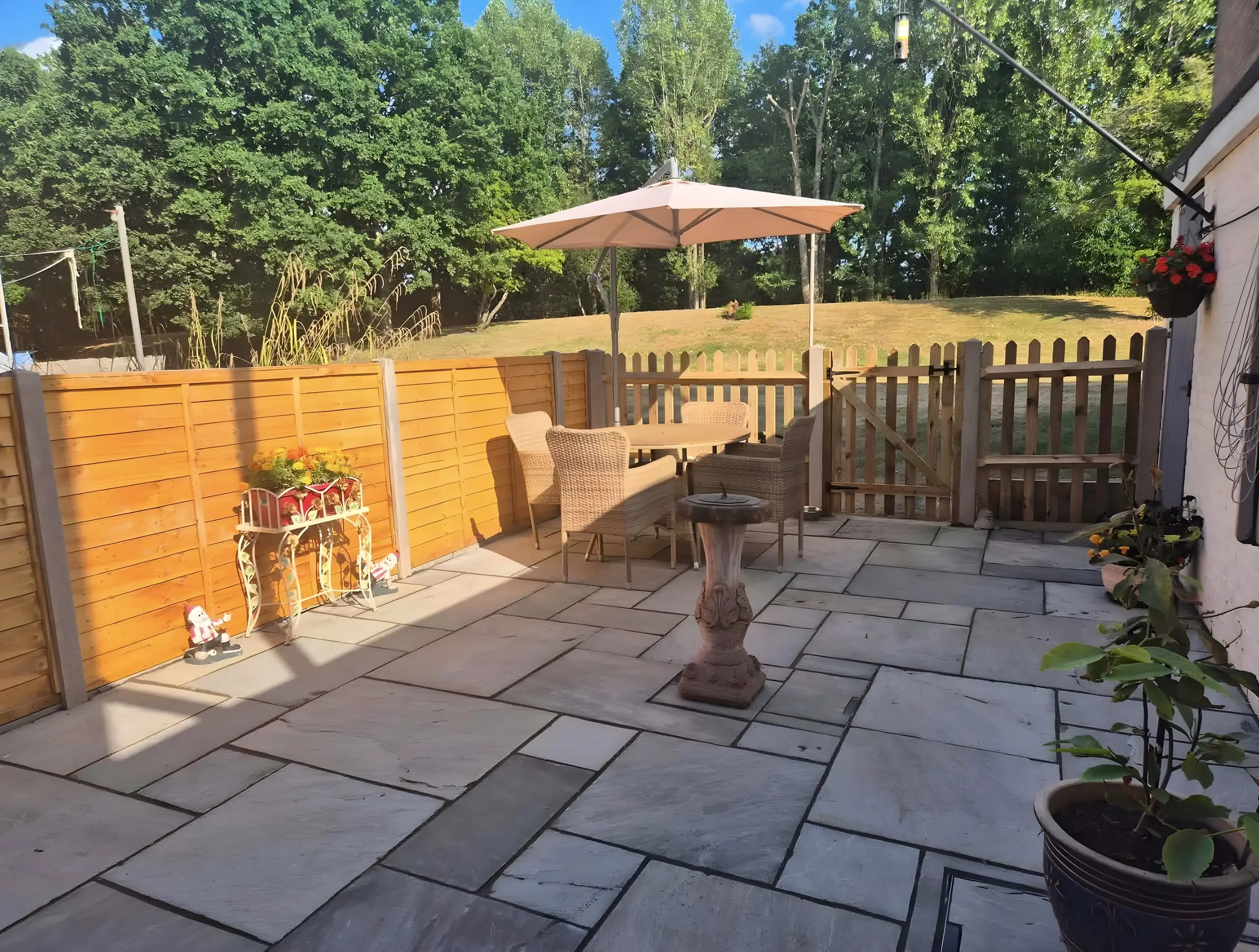 Indian sandstone patio with a parasol and seating, enclosed by a new timber fence