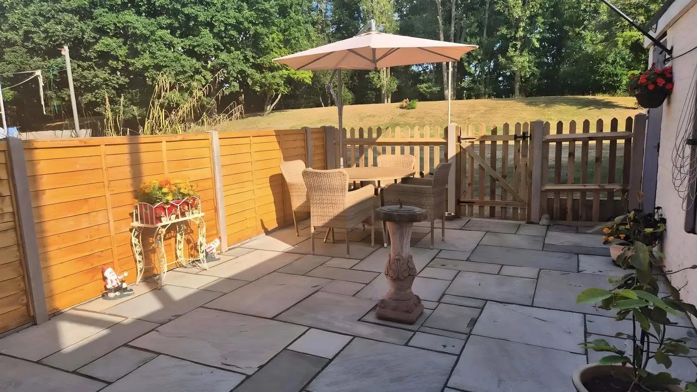 Indian sandstone patio with a parasol, table and chairs, enclosed by a new timber fence
