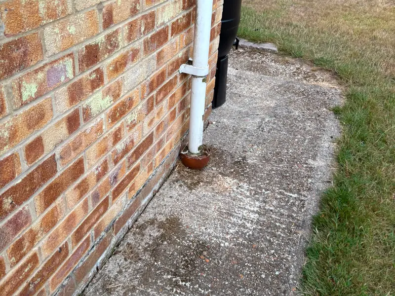 Old stained concrete path and worn lawn beside a brick house wall before work started