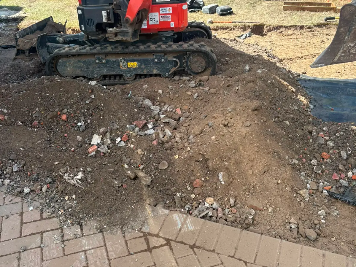 Mini digger excavating the ground beside an existing block paved drive, spoil heaped to one side