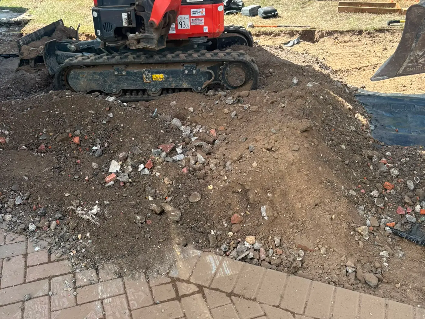 Mini digger excavating the ground beside an existing block paved drive, spoil heaped to one side