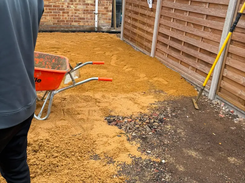 Screeded sand bed laid across the prepared base beside the house and new fence