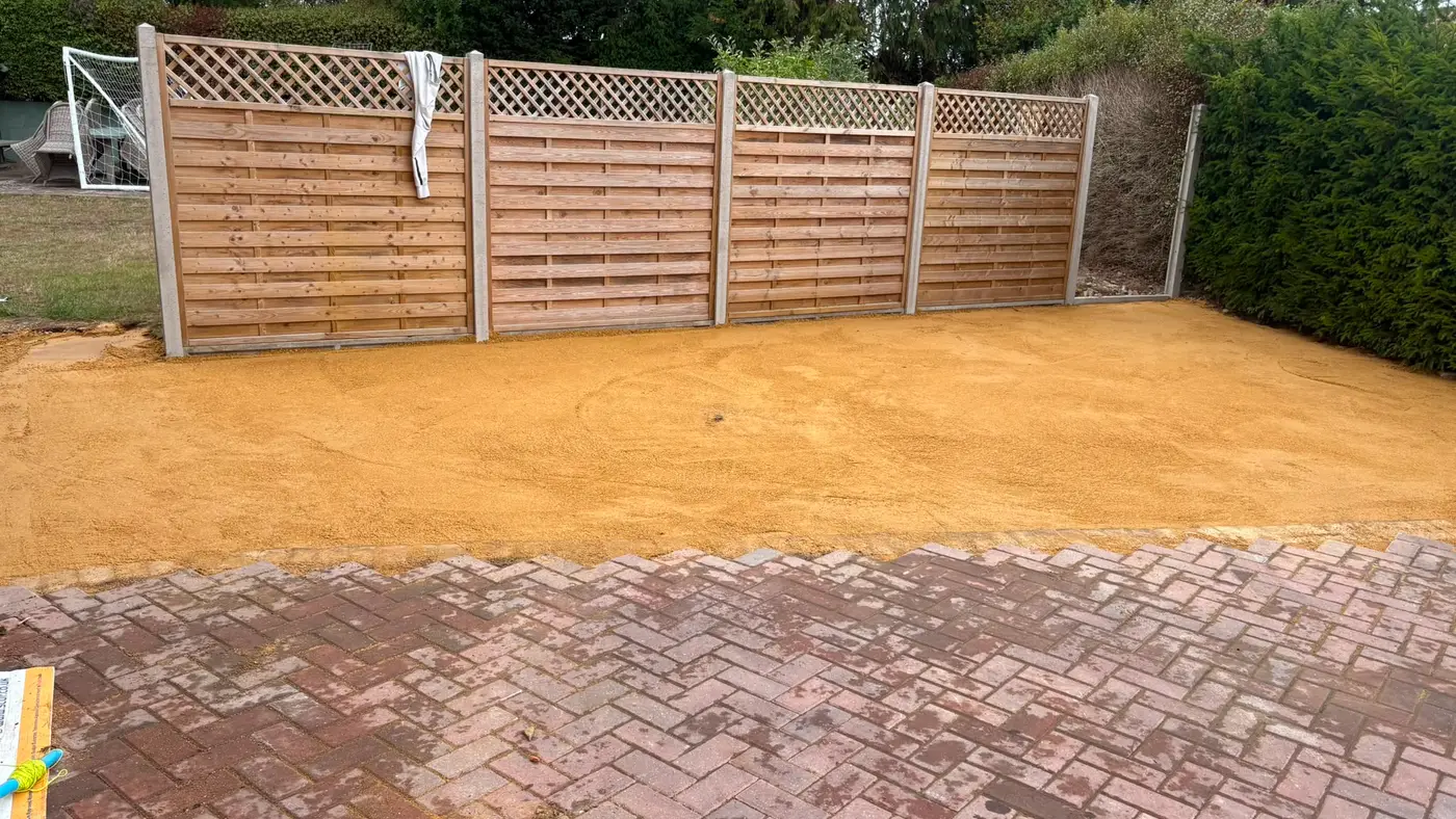 A driveway half finished: laid block paving on one side, screeded sand bed waiting on the other